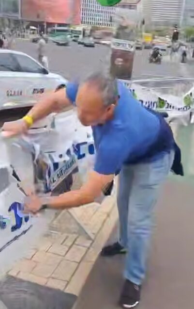 תועד אדם בתל אביב קורע כרזת "עד הנצחון" עם תמונות חיילים שנפלו.